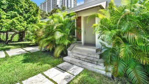 A modern house with a front yard, a staircase leading to the entrance, and a tall building in the background. - Home LifeStyle Miami
Downtown and Miami Beach  (Miami)