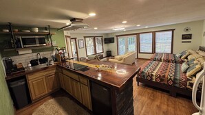 A kitchen with a central island, wooden cabinets, a microwave, and a sink. There is a dining area with a sofa and a patterned rug. - Waterfront Studio with Hot Tub & Fire Pit Sleeps 4 (Eufaula)