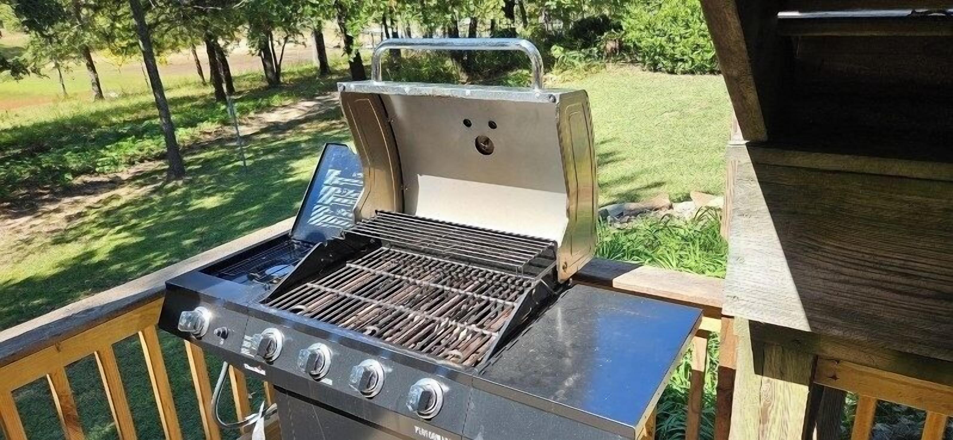 Ein Grill im Freien auf einer Holzterrasse, im Hintergrund eine Rasenfläche.