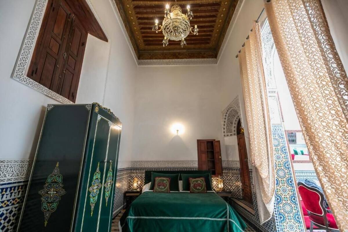 Una habitación con cama, armario de madera, candelabro y paredes con diseño.