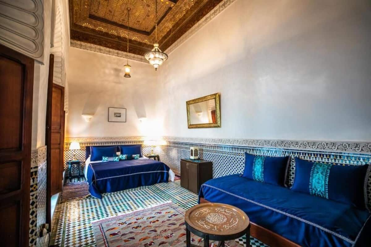 Una habitación tradicional marroquí con dos camas, suelo estampado y techo ricamente decorado.