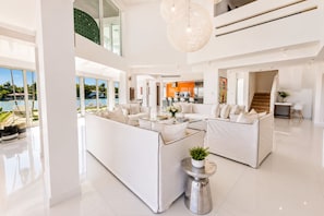A spacious living area with a pool view, white furniture, and a modern kitchen.