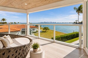 Un balcon avec vue sur l’eau et le panorama de la ville, des meubles en osier et une petite plante en pot.