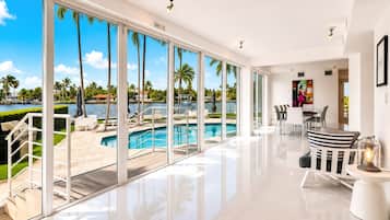 A modern hotel room with a large glass door leading to a pool area, a dining area with a view, and a bright, spacious interior.