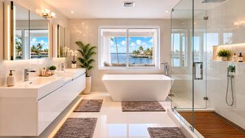 Une salle de bain moderne dotée d’une grande baignoire, d’une douche à parois de verre et offrant une vue sur l’océan grâce à une grande fenêtre.