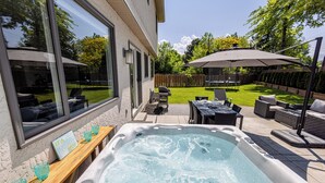 A backyard with a hot tub, outdoor furniture, and a wooden deck.
