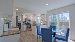 A modern kitchen with white cabinetry, a built-in oven, and a microwave. There is a dining area with blue chairs and a glass table.