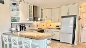 Una cocina con armarios blancos, encimera de granito, campana extractora de acero inoxidable y refrigerador blanco.