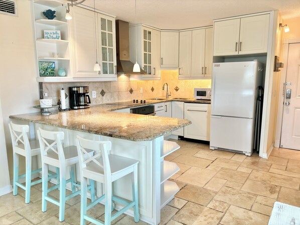 Una cocina con armarios blancos, encimera de granito, campana extractora de acero inoxidable y refrigerador blanco.