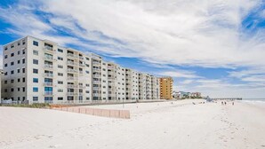 Un hotel frente a la playa con varios pisos, balcones y un muelle al fondo.