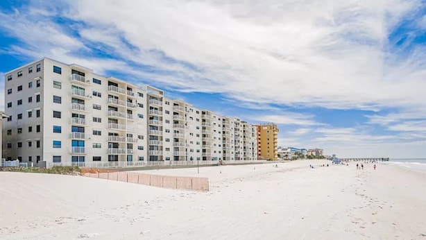 Un hôtel en bord de mer, avec plusieurs étages, des balcons et une jetée en arrière-plan.