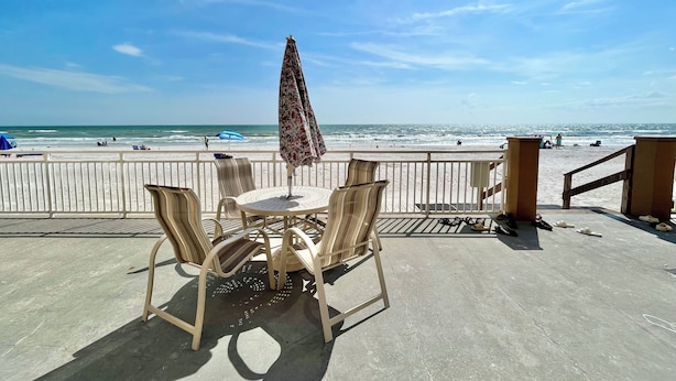 Un patio junto a la playa con una mesa y sillas, con vista al océano.