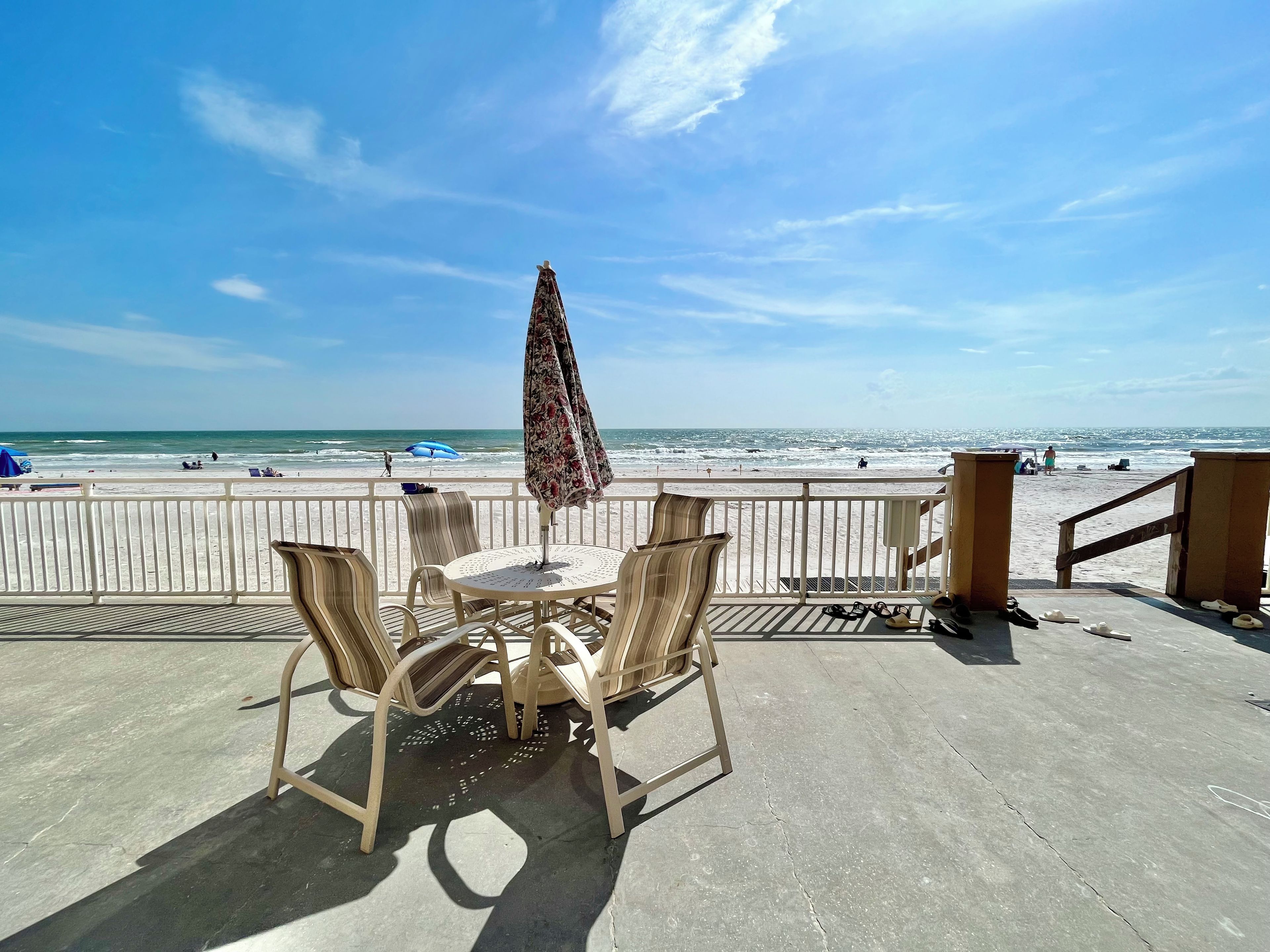 A beachside patio with a table and chairs, overlooking the ocean.