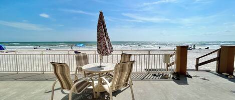 A beachside patio with a table and chairs, overlooking the ocean.