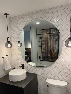 Features a large round mirror, herringbone-patterned backsplash, and sleek countertop.