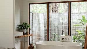 A modern bathroom with a freestanding bathtub, wooden bench, and a large window with a view of greenery. - Boathouse 2 - Hunter Valley Couples Retreat, Bathhouse 2 at Leaves and Fishes (Lovedale)
