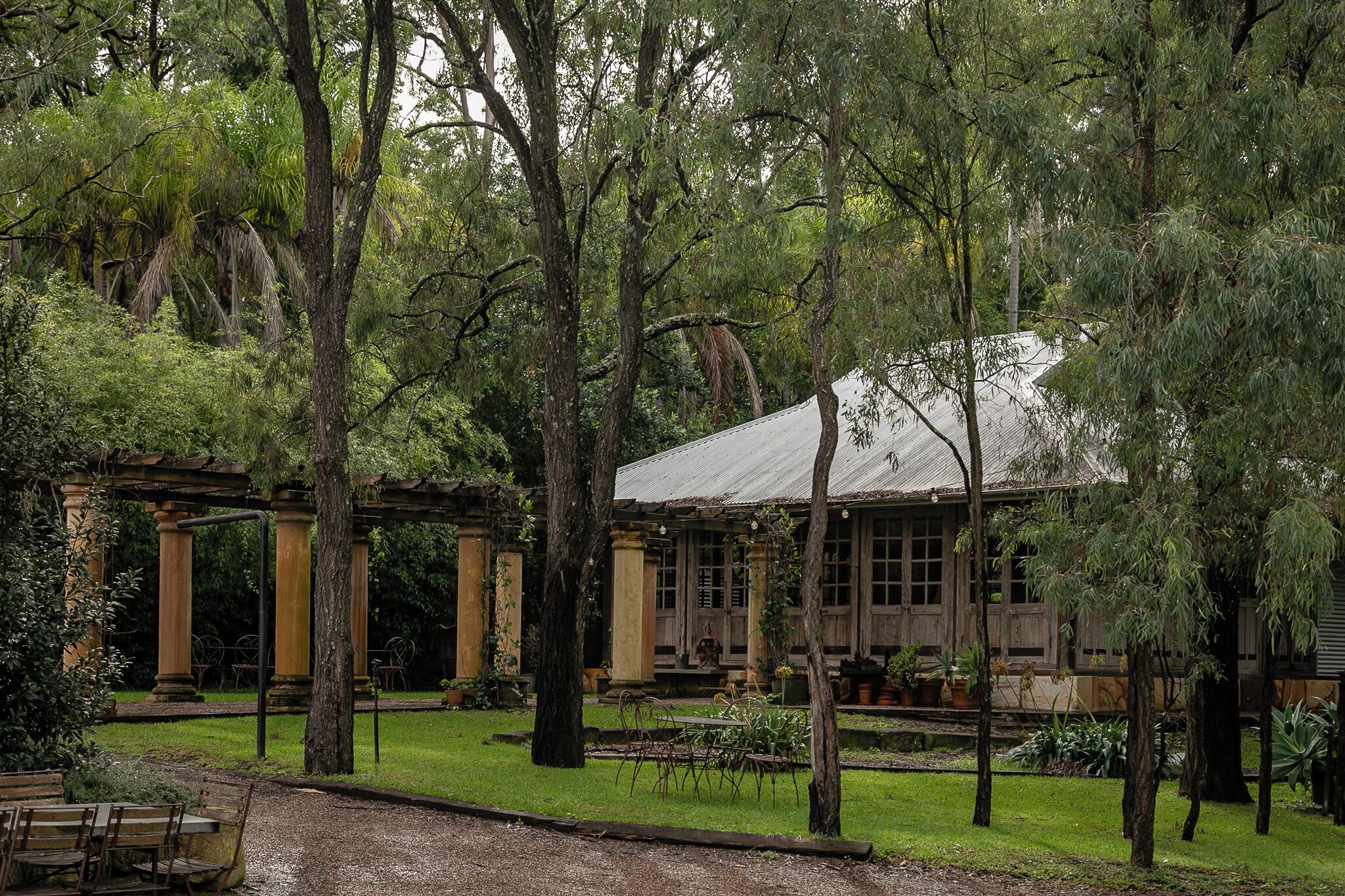 A rustic building with a covered porch, surrounded by lush greenery and trees.