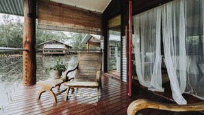 Terraza de madera con banco y planta en maceta, con vista a un cuerpo de agua y edificios.