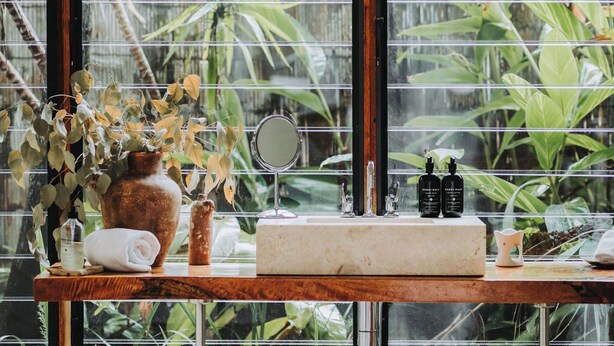 Un baño con una ventana grande, un tocador de madera, un espejo y artículos de aseo.