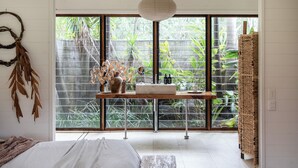 Een moderne slaapkamer met een groot raam, een nachtkastje met een vaas en een geweven mand.