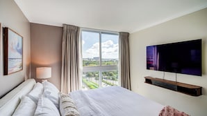 Habitación de hotel con una cama grande, un televisor montado en la pared, una ventana con cortinas y vistas a la ciudad.