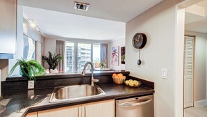 Una cocina moderna con un lavamanos de acero inoxidable, lavavajillas y ventana con vistas a un paisaje urbano.