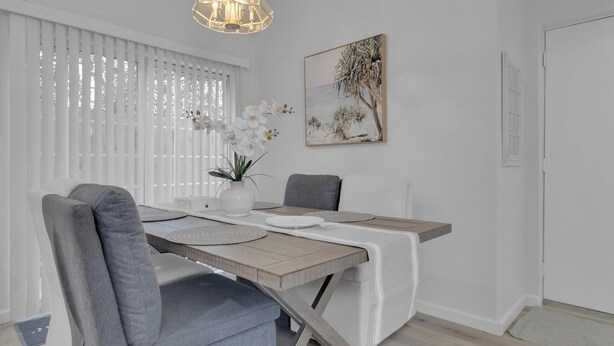 Et spiseområde med et træbord, grå polstrede stole, en vase med hvide blomster og en hængende lampe.