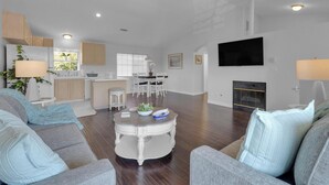 A modern living room with a sofa, coffee table, and TV. There is a kitchen area with cabinets and a dining table. - Bright, Spacious 2BD/2BA in the Heart of Hillcrest (San Diego)