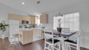 A modern kitchen with wooden cabinets, a white refrigerator, and a dining area with white chairs and a table. - Bright, Spacious 2BD/2BA in the Heart of Hillcrest (San Diego)