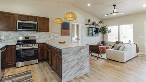 Une cuisine moderne dotée d’un îlot en marbre, d’appareils électroménagers en acier inoxydable, de meubles en bois et d’un coin repas avec un canapé et une plante.
