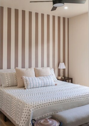 Une chambre à coucher avec un lit, des oreillers, une table de chevet avec une lampe et un ventilateur de plafond.