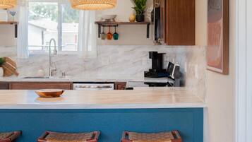 A modern kitchen with a marble countertop, wooden bar stools, and pendant lighting.