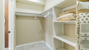 Un placard avec des étagères et une tringle pour suspendre les vêtements, une porte et un sol carrelé.