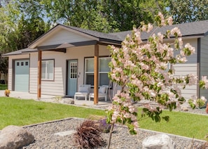Une maison de plain-pied avec un porche abrité, une porte d’entrée et un petit jardin agrémenté d’une plante à fleurs.