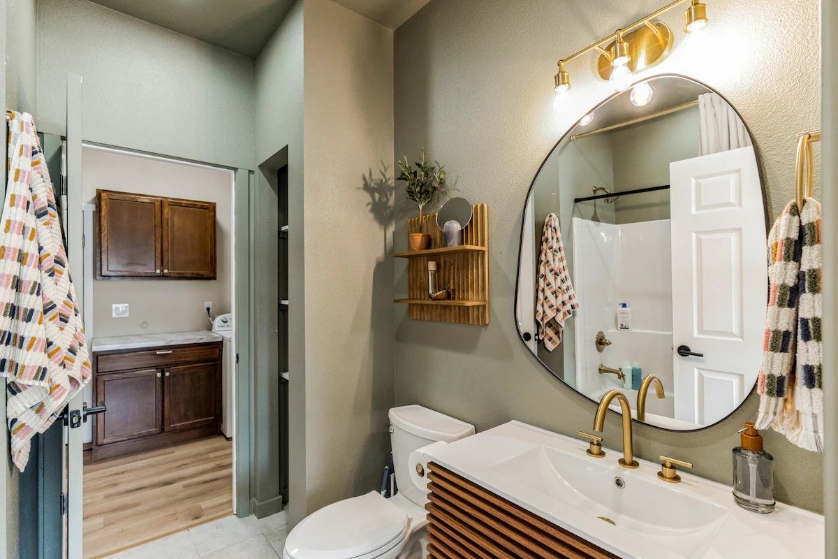 A bathroom with a toilet, sink, and mirror. There is a wooden cabinet and a towel rack.