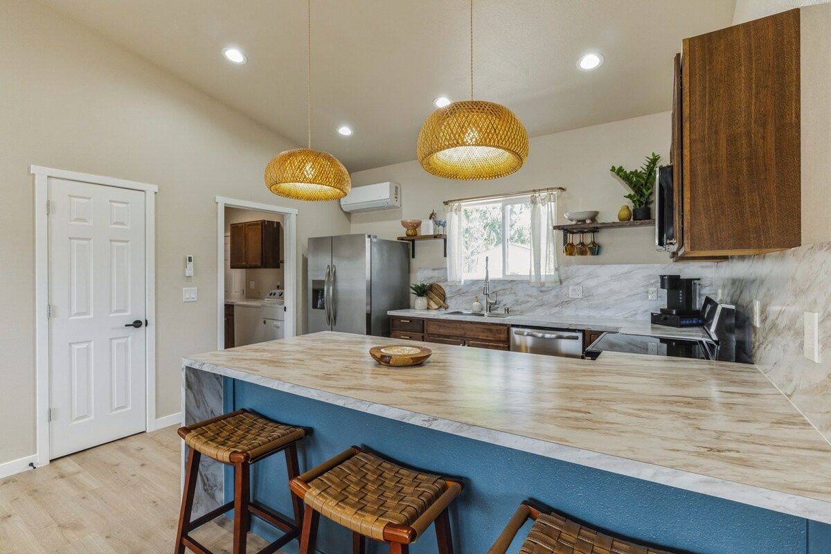 A kitchen with a large island, bar stools, hanging wicker pendant lights, and a built-in oven.