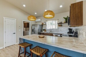 A kitchen with a large island, bar stools, hanging wicker pendant lights, and a built-in oven. - Desert Bliss - Stylish Kennewick Getaway (Kennewick)