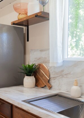 A kitchen with a marble countertop, a sink, a potted plant, a wooden cutting board, and a shelf with a glass object. - Desert Bliss - Stylish Kennewick Getaway (Kennewick)