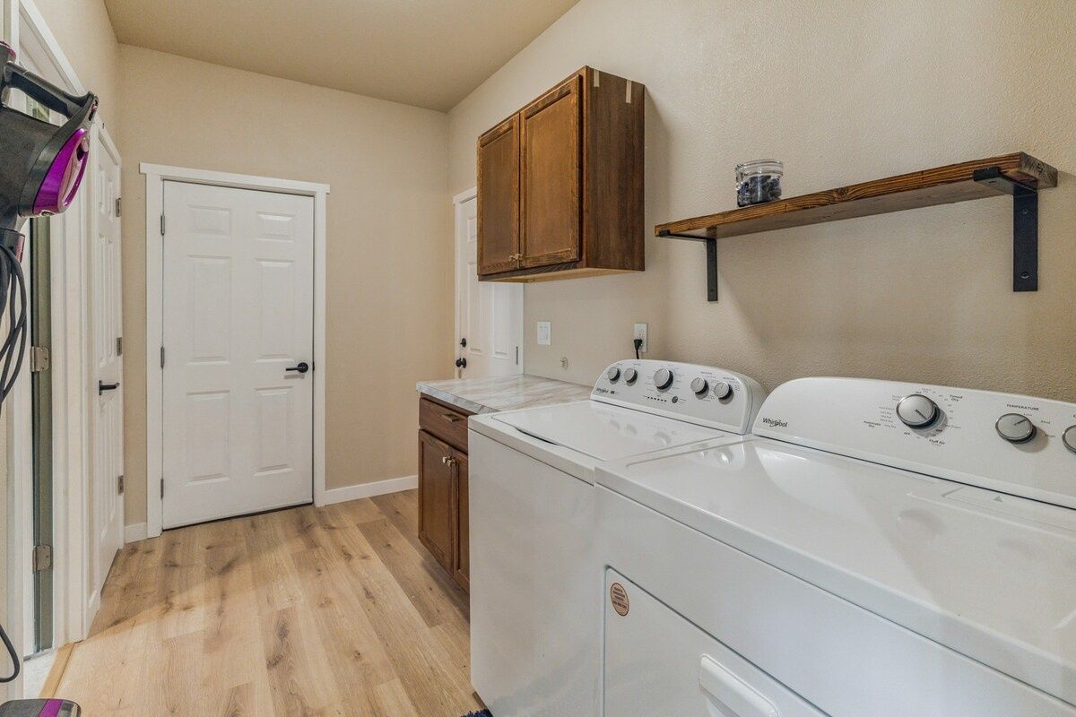 A laundry room with a front-loading washer and dryer, wooden cabinets, and a shelf above the dryer.