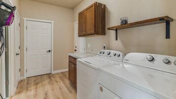 A laundry room with a front-loading washer and dryer, wooden cabinets, and a shelf above the dryer.