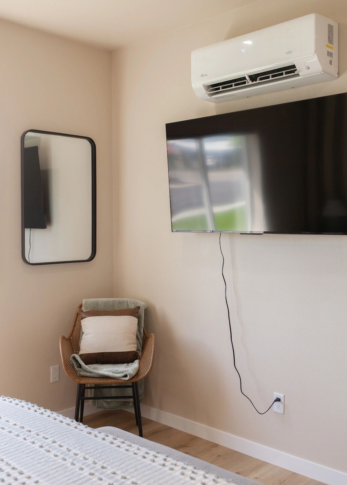 Ein Zimmer mit Wand-Klimaanlage, einem Flachbildfernseher, einem Korbstuhl mit Kissen und einer Steckdose an der Wand.