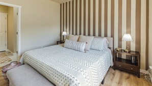 Une chambre à coucher avec un lit, des tables de chevet, un banc et un mur à rayures.