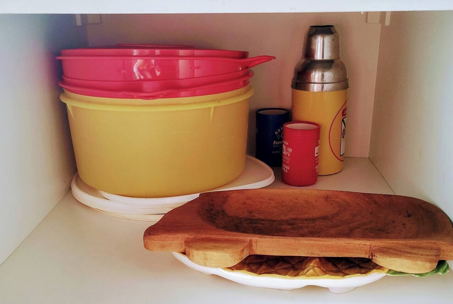 A kitchen shelf with a large yellow container, a red container, a stainless steel bottle, and a red cup.