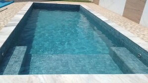 Ein rechteckiger Swimmingpool mit klarem, blauen Wasser, umgeben von einer gefliesten Terrasse.