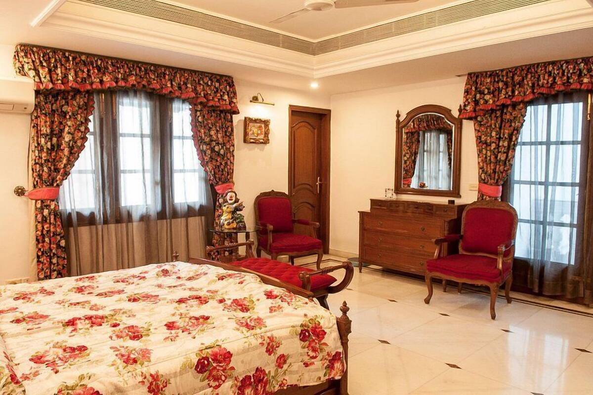 Un dormitorio con colcha estampada, dos sillas rojas, un aparador de madera y un espejo.