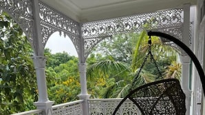 A covered outdoor seating area with wicker chairs and a hanging chair, surrounded by ornate white railings and lush greenery. - VILLA 33 Bed & Breakfast (New Delhi)