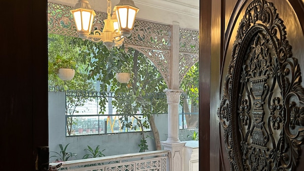 An ornate wooden door with intricate carvings, a balcony with decorative railings, and hanging lantern-style lights. - VILLA 33 Bed & Breakfast (New Delhi)