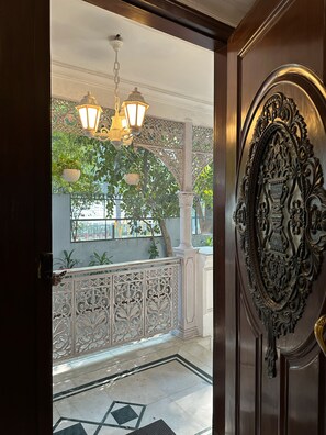 Une porte en bois richement décorée, ornée de sculptures complexes, un balcon avec des balustrades décoratives et des lampes suspendues de style lanterne.