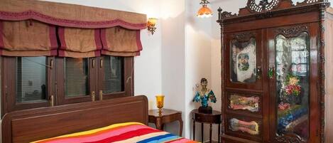 A bedroom with a wooden bed, a colorful striped bedspread, a vintage wooden dresser with glass doors, and a small statue on a side table.