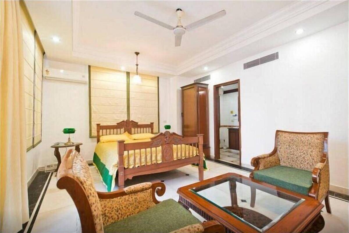 Habitación de hotel con cama, dos sillones, una mesita de centro, ventilador de techo y un espejo.